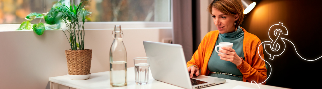 Mujer adulta sentada en escritorio, tomando una bebida y haciendo uso de un computador portatil