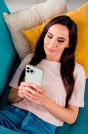 Mujer joven recostada en un sofá usando su celular para simular el ahorro desde una app.