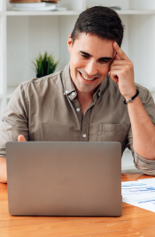 Hombre joven frente a un computador portátil administrando sus ahorros con una sonrisa.