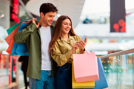 Hombre y mujer en centro comercial disfrutan sus compras mientras consultan descuentos desde el celular con la Tarjeta FEPEP. Ahorro, beneficios y conveniencia.