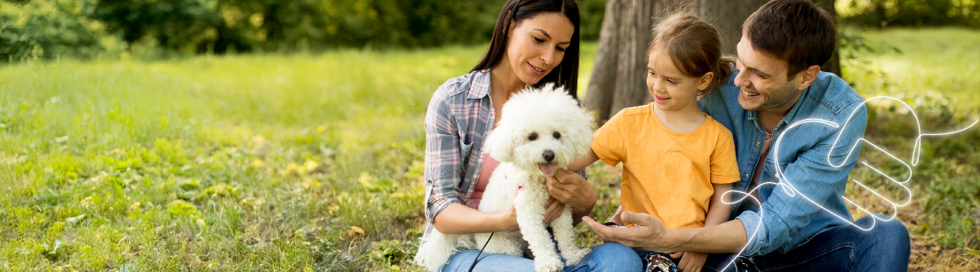 Familia feliz disfrutando de un momento al aire libre con su mascota, una perrita blanca. La madre y el padre están sentados en el césped junto a su hija, sonriendo y acariciando al animal. El entorno es un parque verde y soleado, lo que crea un ambiente acogedor y relajado.