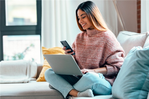 Mujer joven gestionando sus finanzas desde casa con laptop y celular, reflejando el beneficio del aporte social y permanente en FEPEP.