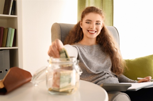 Mujer joven depositando dinero en un frasco de ahorros en casa, representando el hábito de ahorro programado ofrecido por FEPEP.