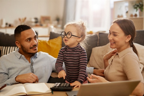 Niña con gafas jugando con una calculadora junto a sus padres, representando la educación financiera en familia promovida por FEPEP.