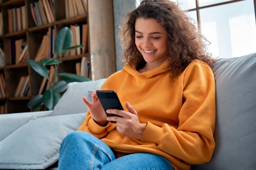 Mujer joven sonriendo mientras usa su celular en casa, simbolizando la facilidad de gestionar un CDAT digital desde cualquier lugar.