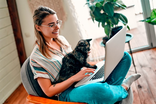 Mujer joven con su gato en casa, participando en actividades de ahorro voluntario a través de su computador portátil.