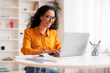 Mujer sonriente trabaja en su computador portátil desde casa, accediendo fácilmente a los términos y condiciones del portal FEPEP.