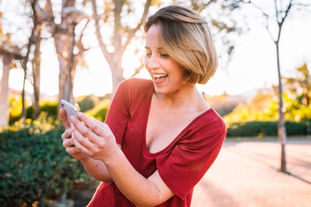Mujer feliz revisa su celular en un parque, representando el acceso fácil y rápido a información sobre tasas de ahorro desde cualquier lugar.