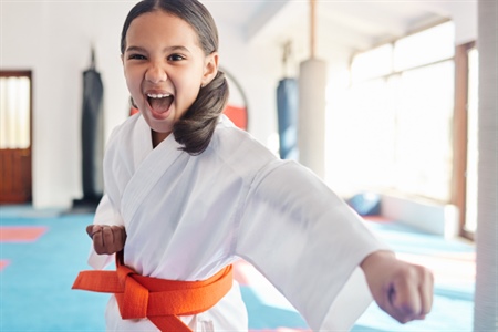 Niña con uniforme de artes marciales y cinturón naranja practicando con entusiasmo.