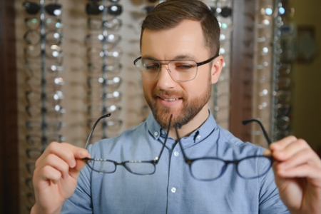Hombre joven comparando gafas en una óptica, cuidando su salud visual.