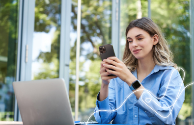 Mujer joven usando su celular al aire libre frente a su portátil, simbolizando comodidad y acceso rápido a consultas digitales.