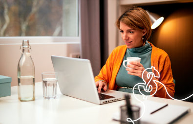 Mujer feliz revisa su celular mientras usa su computador portátil, ideal para ilustrar la consulta de tasas de CDAT de forma digital.